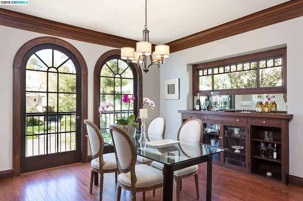 This dining room featuring white walls and hardwood flooring, along with a modern dining table set light by the attractive modern chandelier.