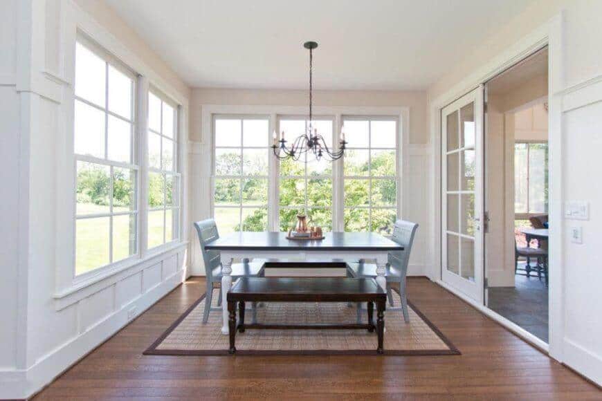 Classy dining room with wooden table and a pair of wooden bench and chairs brighten by a chandelier. This room has white walls and a window with a great view.