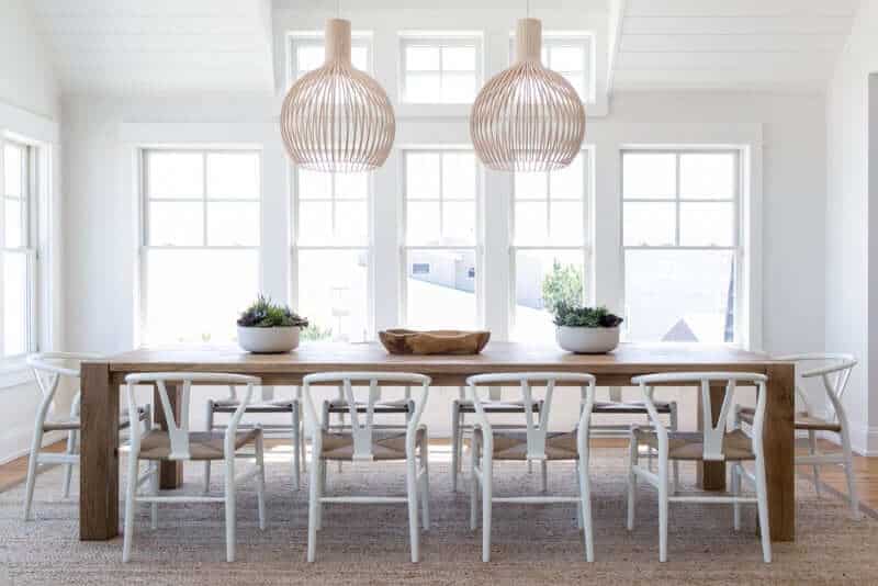 White dining room with wooden tables pair with white chairs on the rug. This room features a white ceiling and white walls with a window.