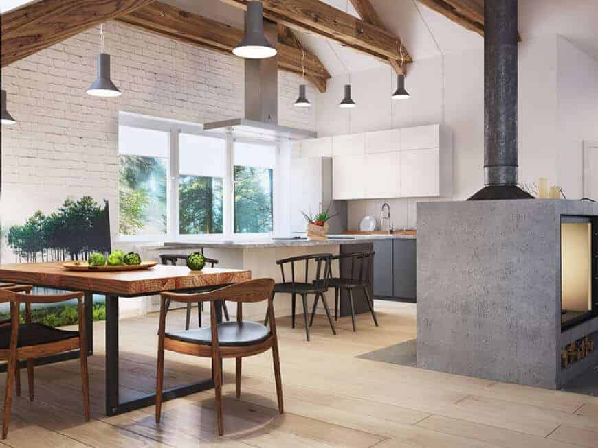 This kitchen has a great combination of rustic and modern with its white island and shelves, brown and black dining chairs, wooden dining table, and grey fireplace, while the light wood flooring gives a fresh, vibrant look to the kitchen without messing up the color scheme. The beam ceiling also makes the room look bigger.