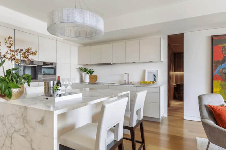 This modern kitchen has a subtle tropical feel to it with the all-white interior and indoor plants. The marble island and the chandelier complete the modern design.