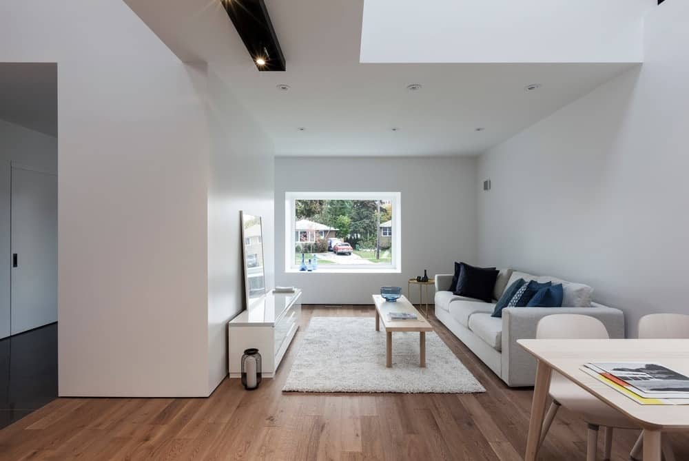 The small white living room features a classy sofa set on the top of hardwood flooring. There's a window with a view outside of the house.