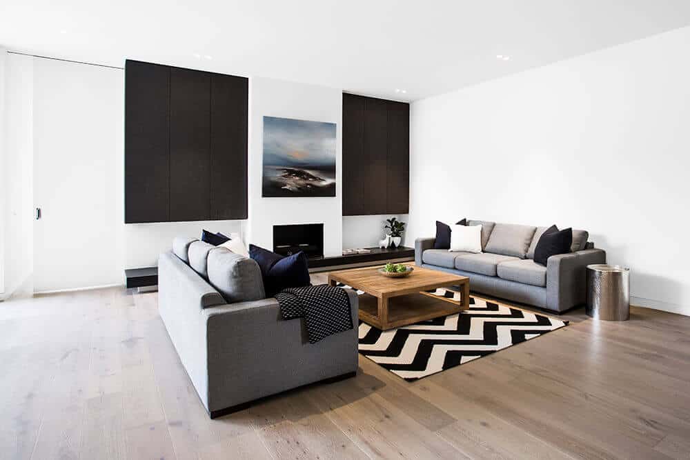 Classy living room design with a comfy couch and wooden table on the rug. This room also has white walls with decor and hardwood flooring.
