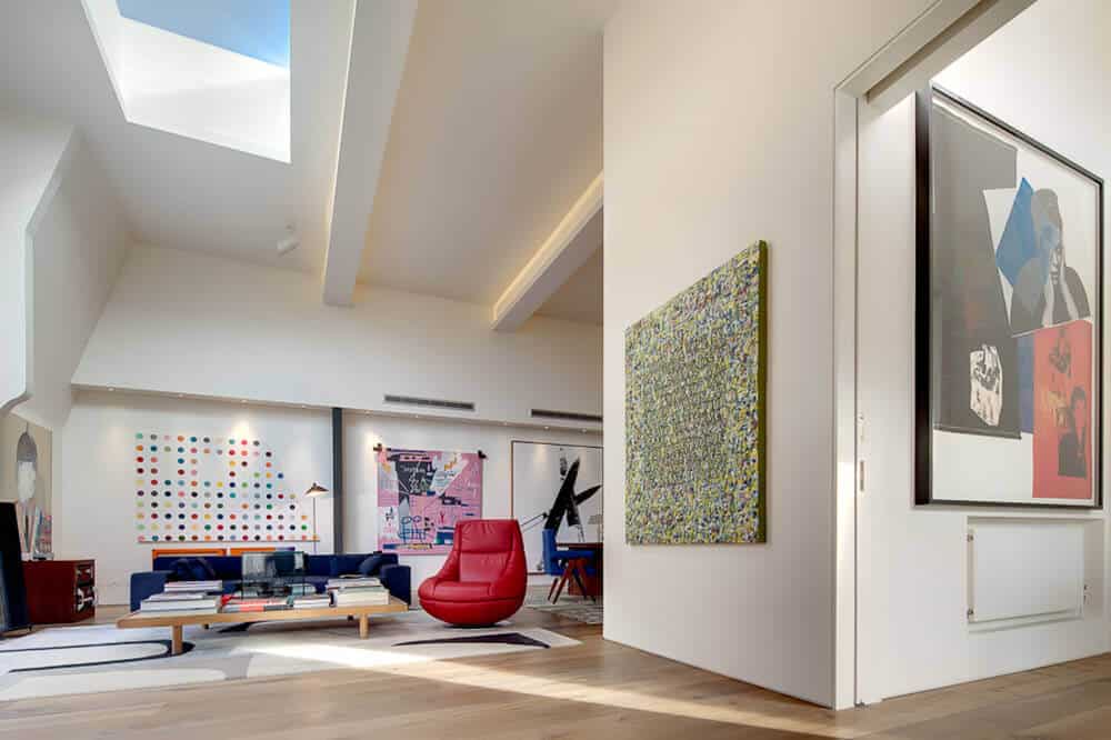 Large living room with attractive red couch and multiple walls decor. This room has hardwood flooring and a blue sofa set and a wooden table on the rug.