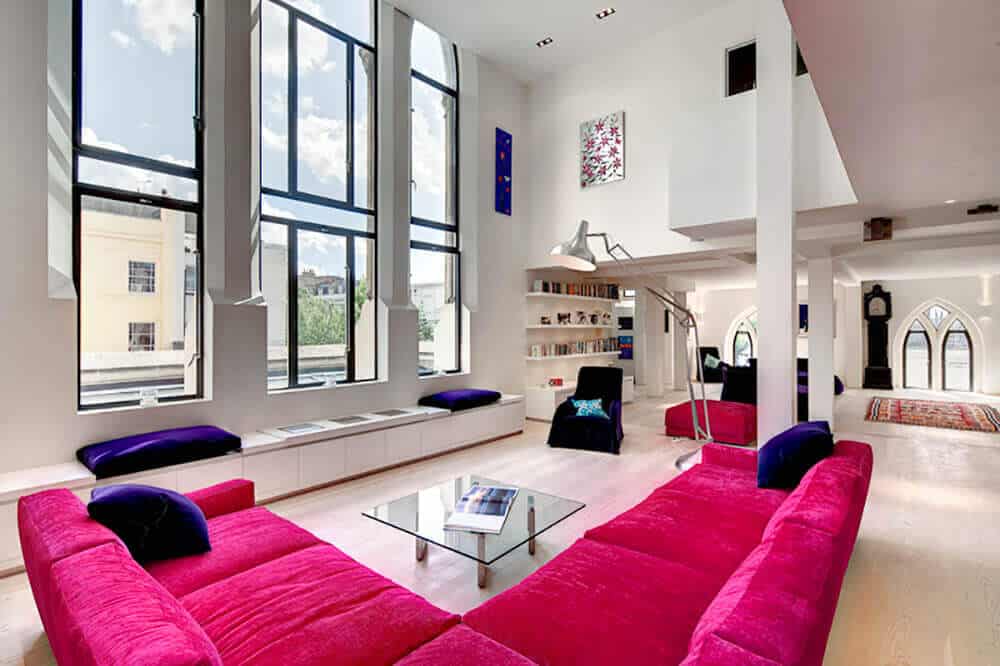 This living room featuring hardwood flooring a classy pink sofa set in front of the glass window. The room also features a stunning high ceiling.