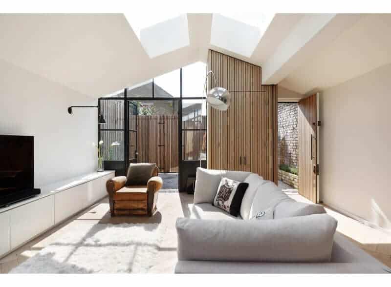 This modern living room features a stunning sofa set in front of the TV. This room also has white walls and a wooden door leading to the porch.