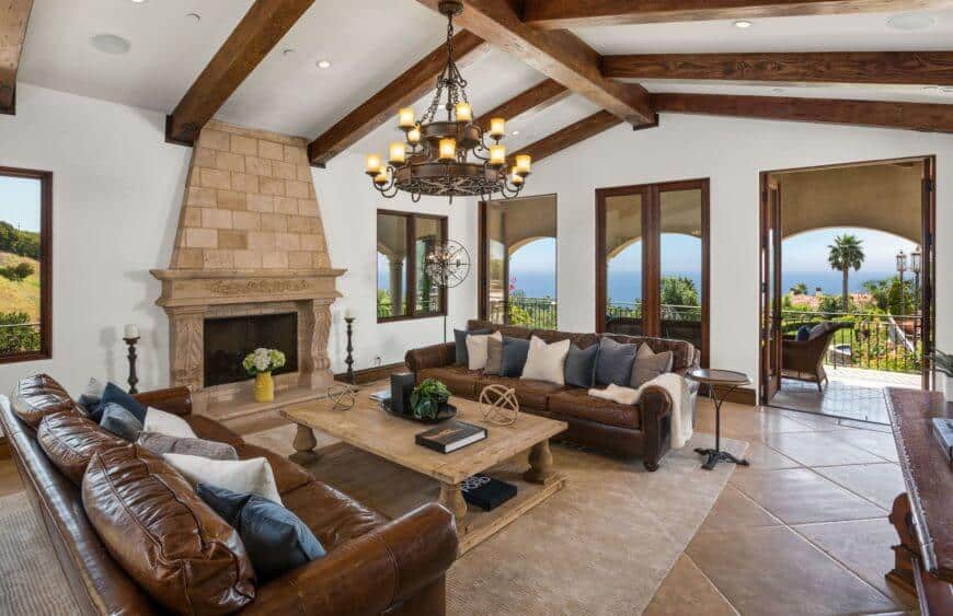 A Mediterranean home highlighting a living room with an classic sofa set and wooden table on the carpet. This room also has a classy fireplace lighted by a stunning chandelier.