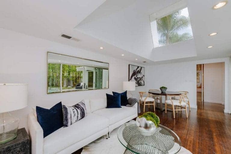 Small white living space features classy hardwood flooring and white vaulted ceiling. This room also has a dining space with a round table set and wooden chairs.