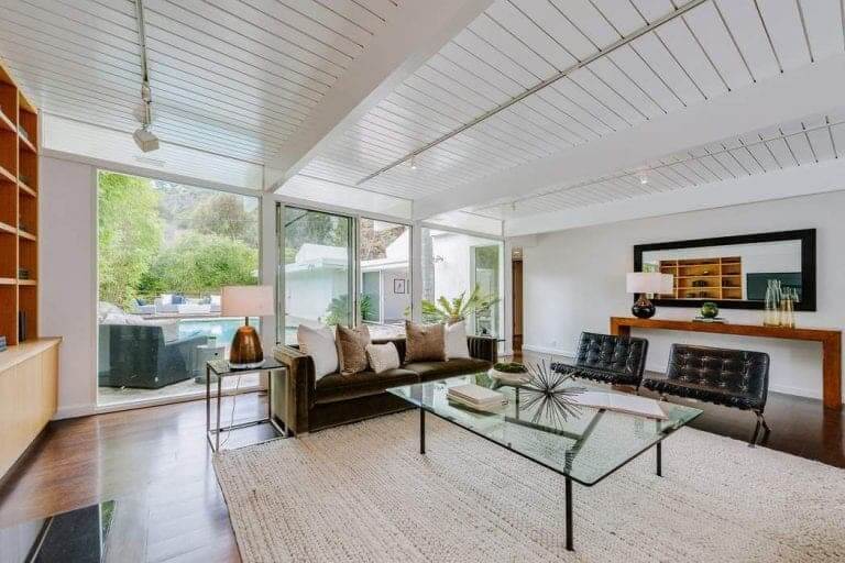 A formal living space highlighting modern sofa set with glass table on the rug. This room also has a glass window with a swimming pool view outside.