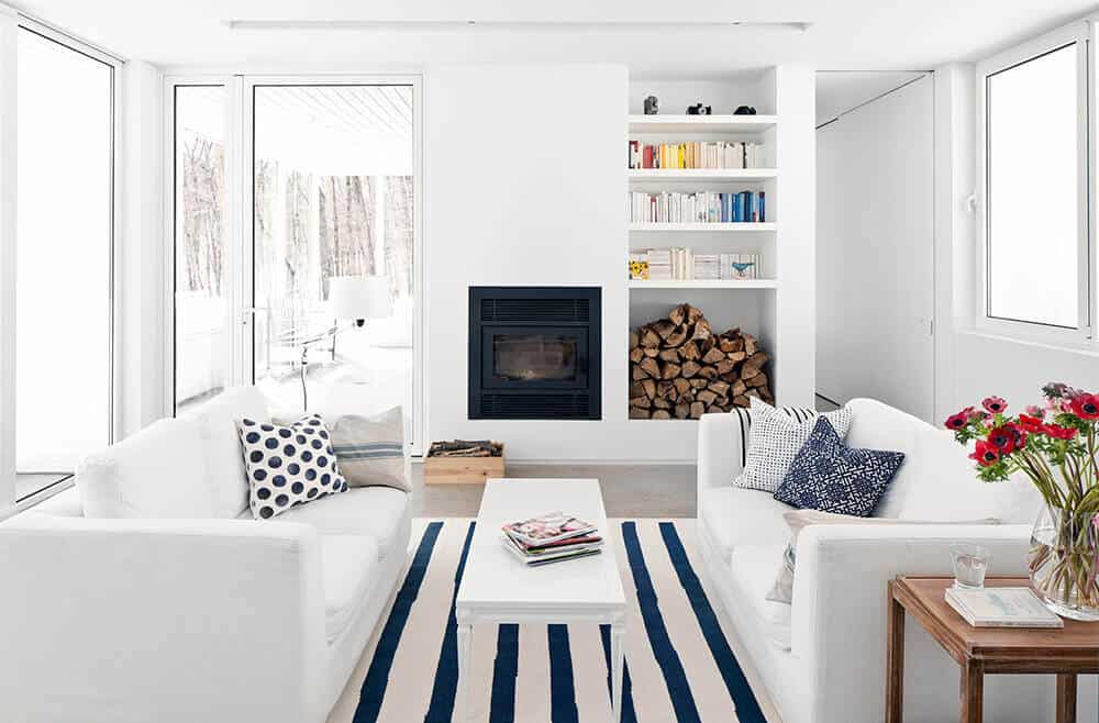 Bright living space with white walls and ceiling coordinated by white sofa set and white rectangular table on top of the carpet. This room also has a fireplace.