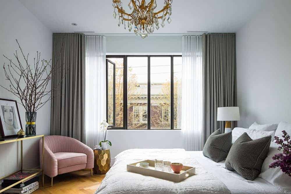 Master bedroom highlighting herringbone-style hardwood floors with an accent of gray window curtains. And the room is lit by an alluring light fixture.