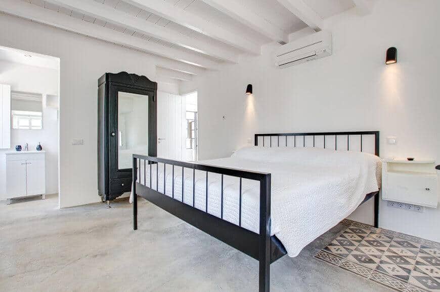 A master bedroom that flaunts carpet flooring, white walls with divider sconces and a white ceiling with uncovered shafts. The bed frame is simple yet classy with a little hanging side table and an accent closet.