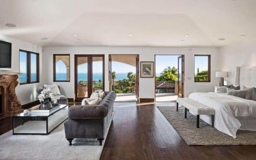 Large master bedroom including entryways leading to a large balcony area. The room flaunts its own living space arrangement with a fireplace and a TV.