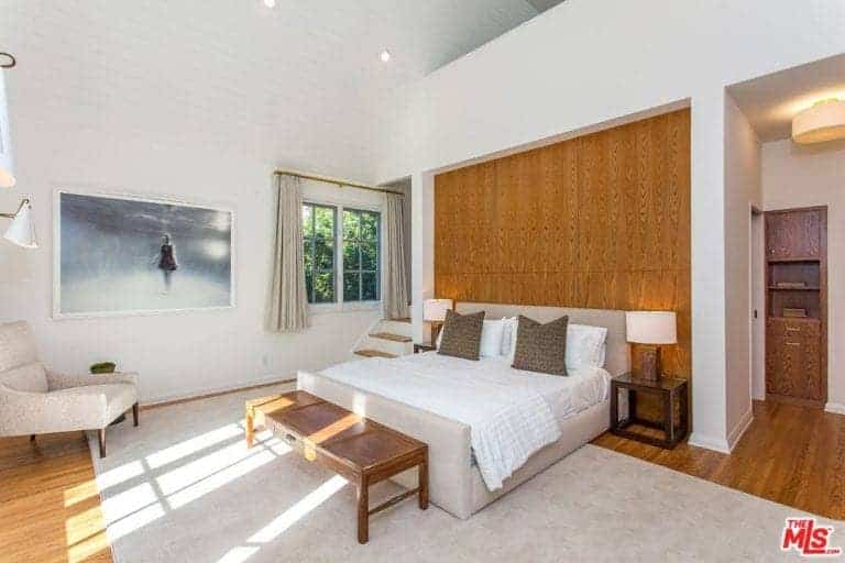 A master bedroom highlighting a comfortable bed with two table lights. The white walls also feature gorgeous wall decor.