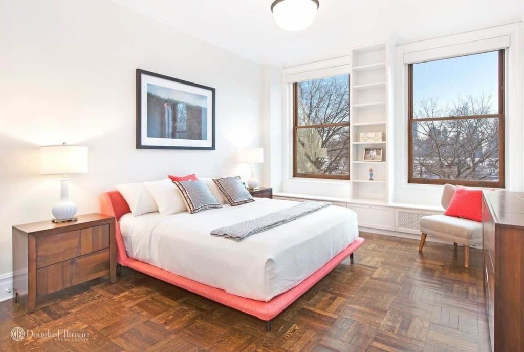 This master bedroom has a pink-framed bed surrounded by white walls with built-in shelving.