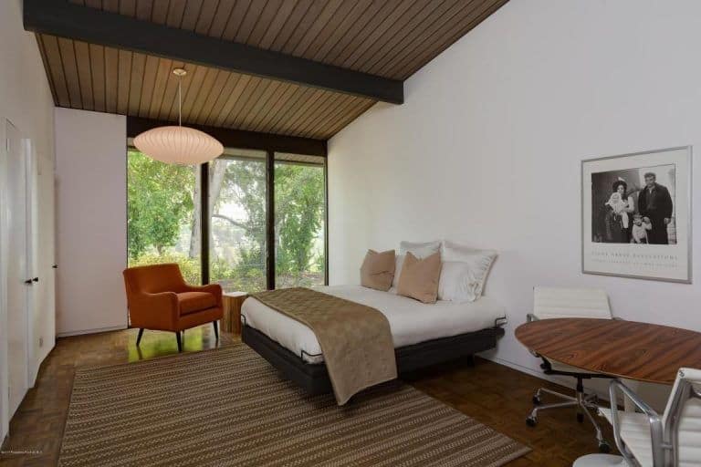 Master bedroom highlighting classy hardwood floors and rustic ceiling with exposed beams. There's a round table with a modern chair on the side.