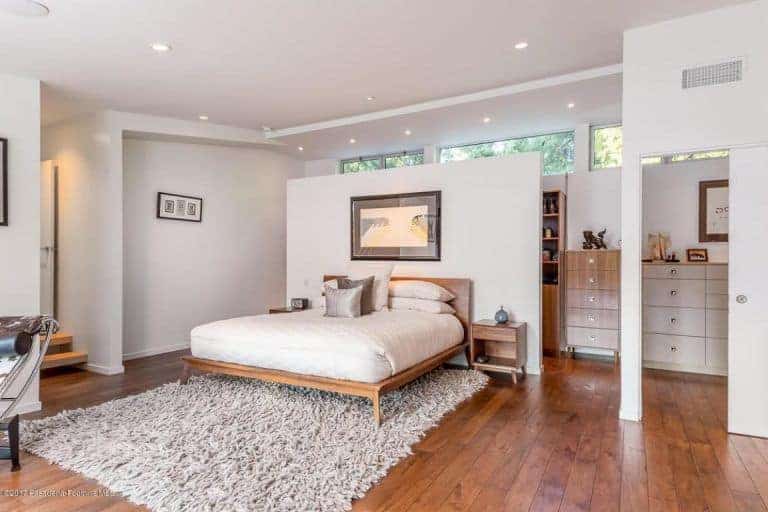 The master bedroom looks gorgeous with dispersed recessed lights on the white ceiling. The hardwood flooring combined altogether with white walls and the carpet matches with the bed perfectly.