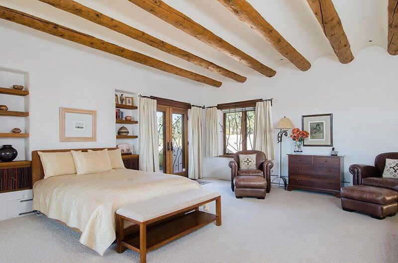 A carpeted white bedroom that highlights roof bends with wood beams promoting acoustic and stylish sense.