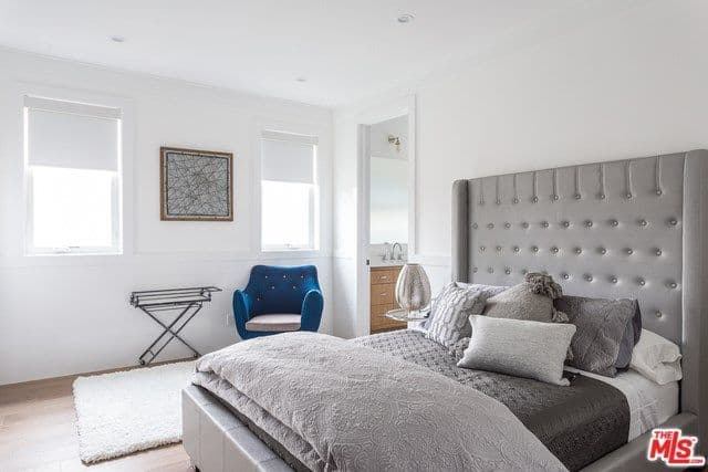 This master bedroom has a monochromatic gray bed design surrounded by white walls and ceiling and has a cute little blue side chair that stands out.