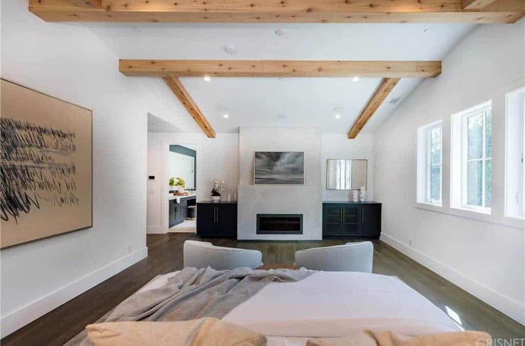 This master bedroom has its own washroom. The bedroom highlights white walls with wall decor and a white ceiling with exposed beams.