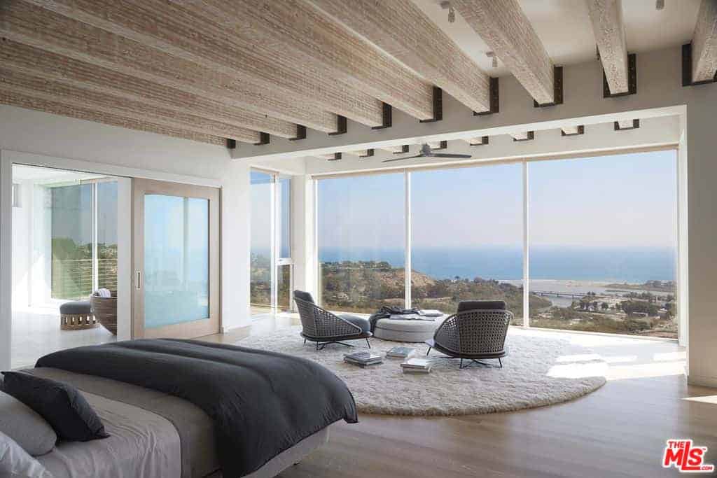 A large modern master bedroom including a couple of stylish chairs and a white couch by the windows. The room also has creative wall decors.