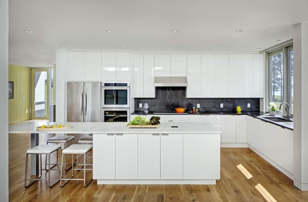 Large, spacious, and fresh are just a few terms that fit the style of this kitchen. It has a generous and long white peninsula with four chairs ready underneath, a white counter with sink, with a touch of black marble pattern on the splashback, while the two-door fridge makes for sturdy storage for fresh ingredients. It would be a delight to cook during the daytime with the sunlight streaming in through the glass window by the sink.