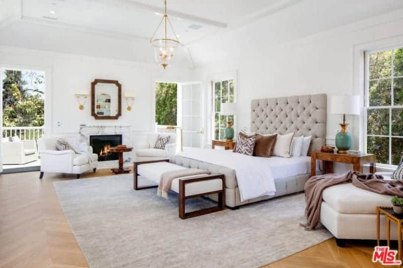 This master bedroom features hardwood flooring and a large carpet. The room has a fancy bed and sitting area by the fireplace.