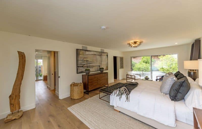 This master bedroom featuring hardwood flooring and a king-sized bed. The room also offers a comfy seating area with a large glass window and a great view outside.