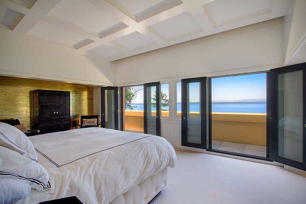 A master bedroom featuring white carpet floors and white walls along with a white ceiling. There are doorways leading straight to the balcony patio.