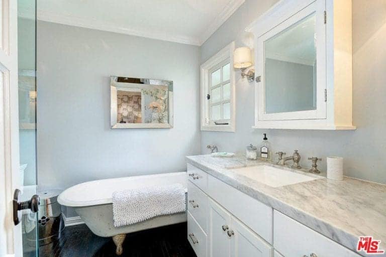 Modern primary bathroom with fancy clawfoot tub and a white sink vanity topped with a medicine cabinet and classic wall sconce.