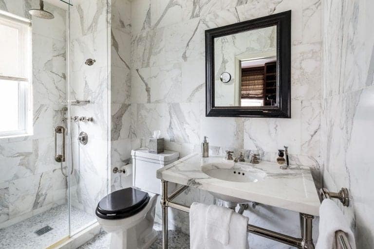 The marbled bathroom offers a drop-in bathtub and mirrored sink vanity topped with a quartz counter and paired with a glam mirror lighted by a vintage wall sconce.