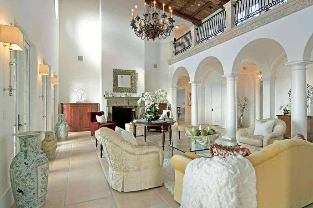 This mansion offers a modern living room with cozy seats and a fireplace set on tiles flooring under the high vaulted ceiling brightens by a stunning chandelier.