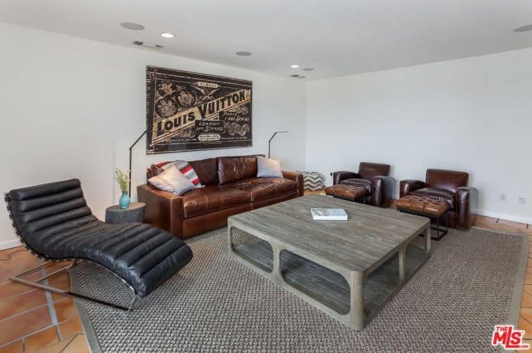 A small living room boasts a brown sofa set and a wooden table on the carpet. This room has a white wall with huge wall decor.