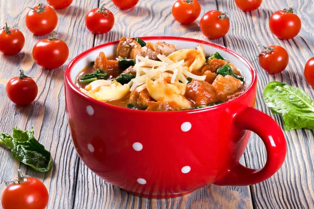 A bowl of creamy spinach and Italian sausage soup with tomatoes on the side.