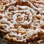 A plate of freshly made funnel cake with powdered sugar on top.