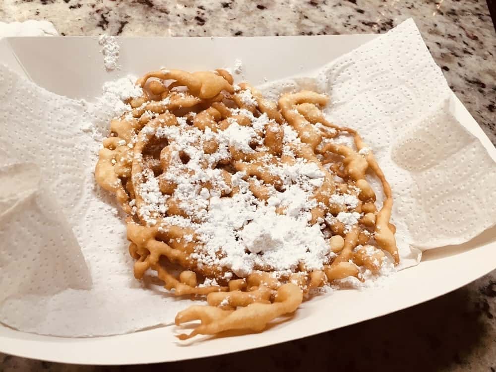 A plate of homemade funnel cakes with white sugar on top.