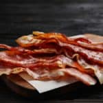 Slices of crispy fried bacon on a chopping board.