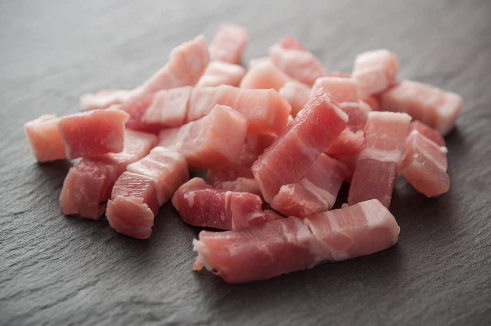 A close look at pieces of lardon bacon on a dark surface.