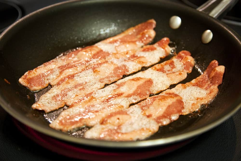 Slices of turkey bacon being fried on a pan.