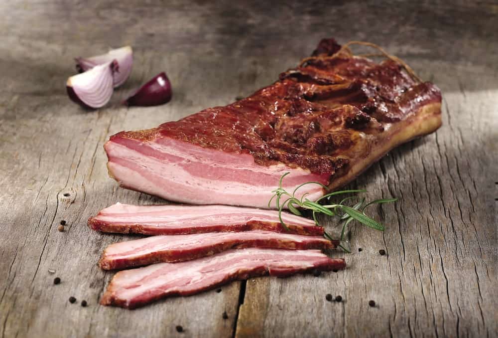 Freshly-made bacon with spices on a wooden table.