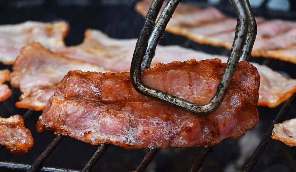 Pieces of bacon being cooked on the grill.