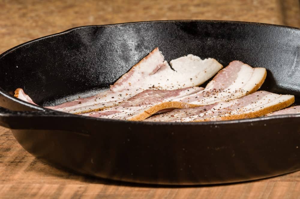 Slices of bacon on a cast-iron skillet.