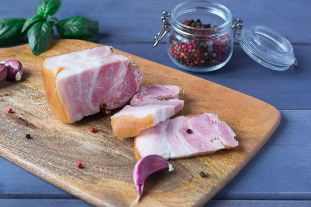 Freshly-made bacon with spices on a chopping board.