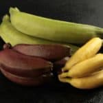 Three varieties of colorful bananas on a dark surface.