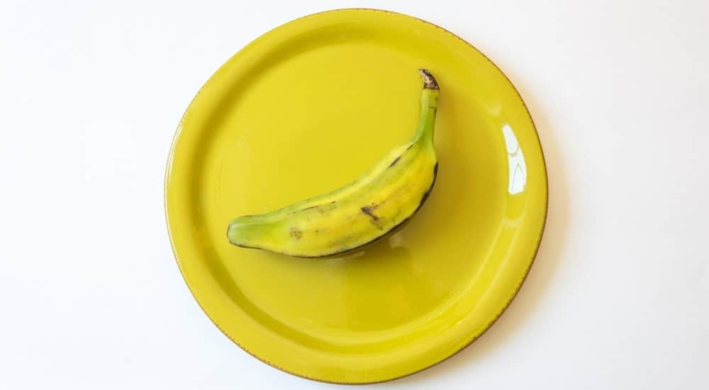 A half ripe burro banana on a yellow plate.
