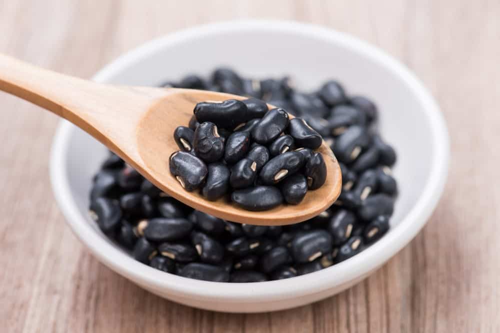 A close look at a bunch of black beans scooped by a wooden spoon.