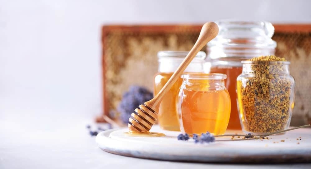 A glass jar of granulated honey along with other types of honey in glass jars.