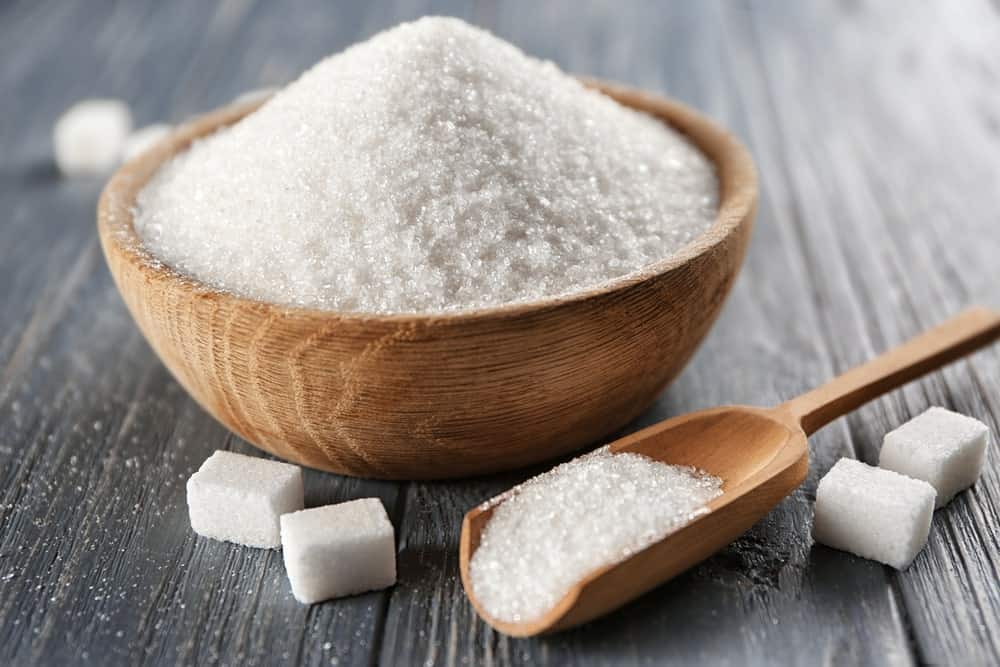 A wooden bowl of sugar along with sugar cubes.