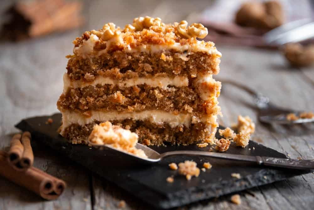 A look at a slice of carrot cake that is topped with walnuts.