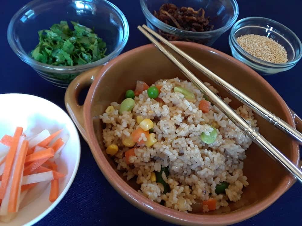 A bowl of freshly cooked vegan fried rice with topping options on the side.